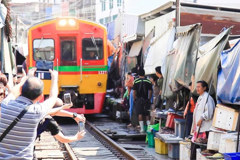 Toursit Taking Photo Of The Approaching Train At Maeklong Railway Market Near Bangkok